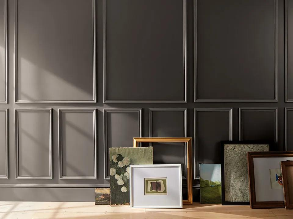 Artwork and frames arranged against a wall painted in Benjamin Moore Silhouette AF-655 with panel moulding